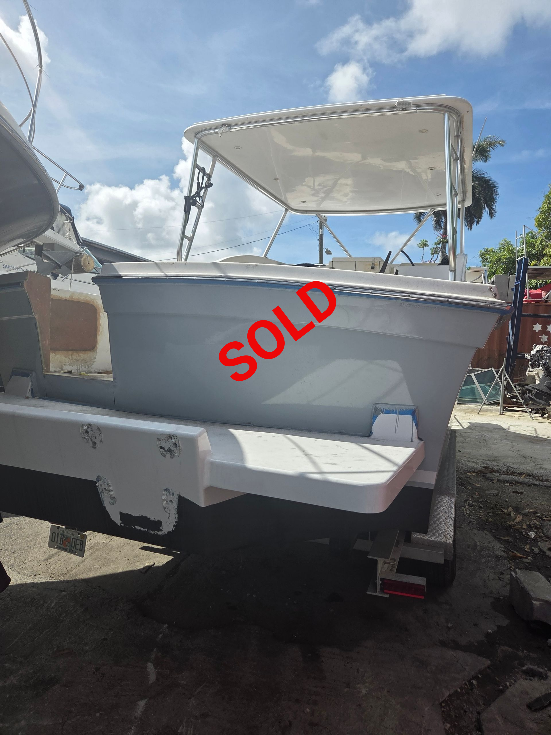 White and gray boat on a trailer, under a blue sky, with a white canopy.