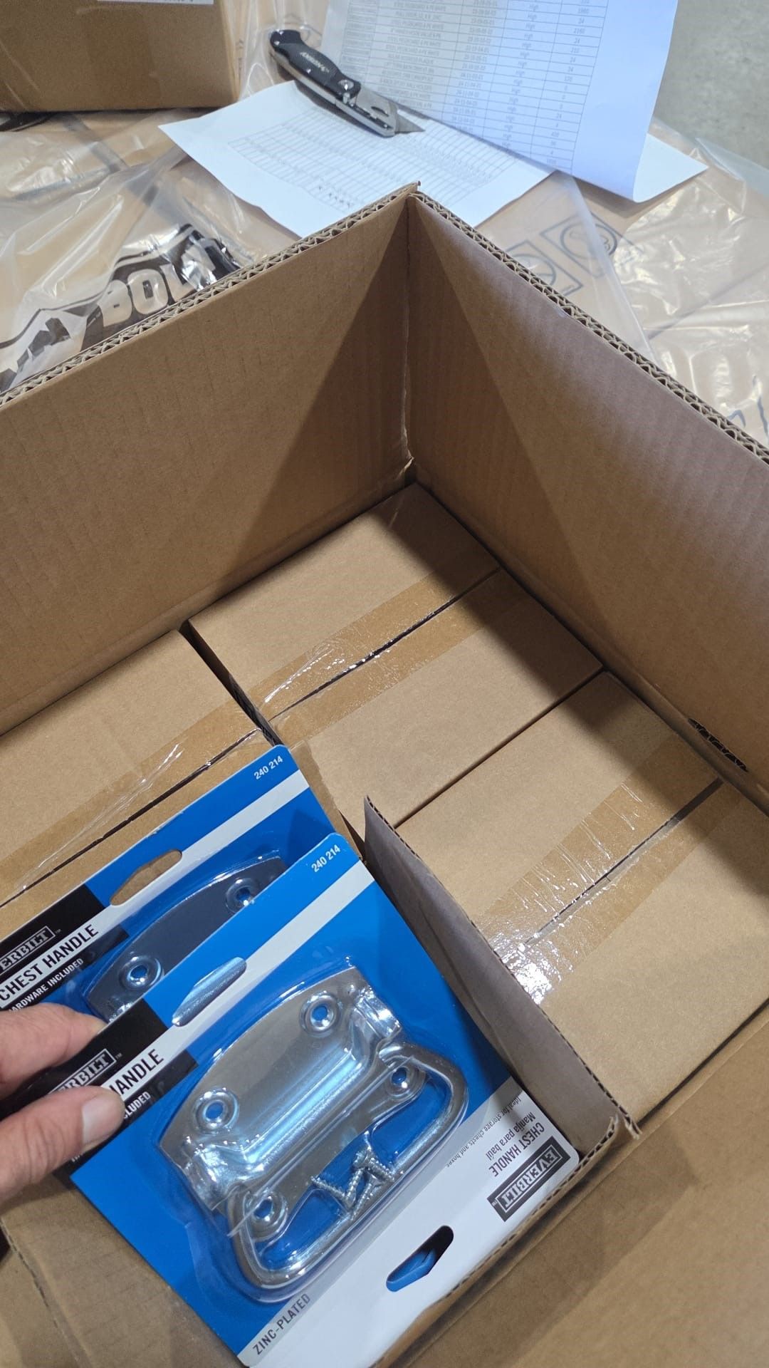 A person's hand holding a metal handle package in a cardboard box filled with smaller boxes.