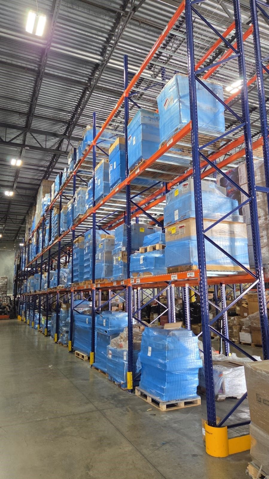 Warehouse with tall blue and orange shelving stacked with wrapped pallets.
