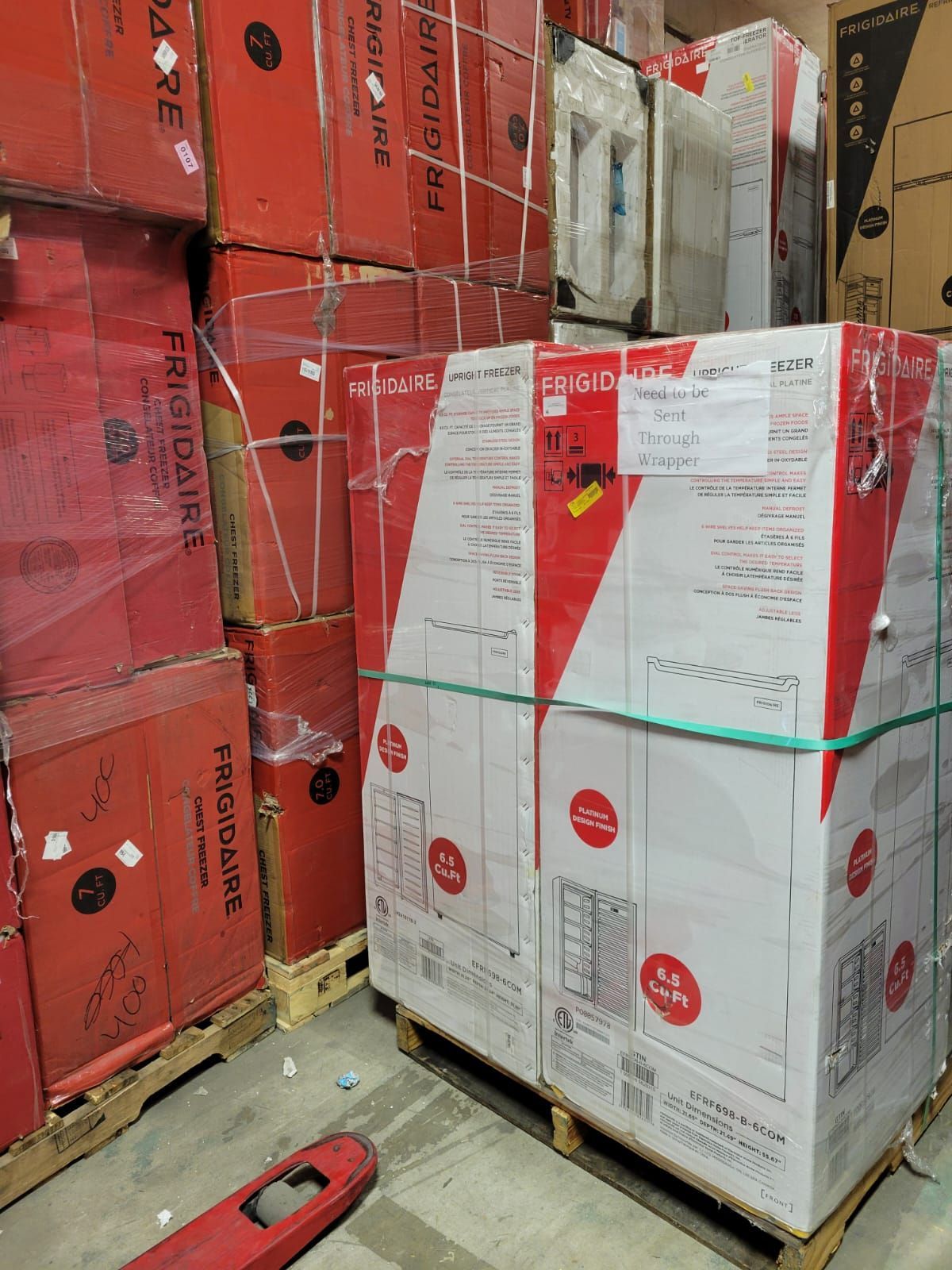 Stacked Frigidaire appliance boxes on pallets in a warehouse, some red, some white, secured with straps.