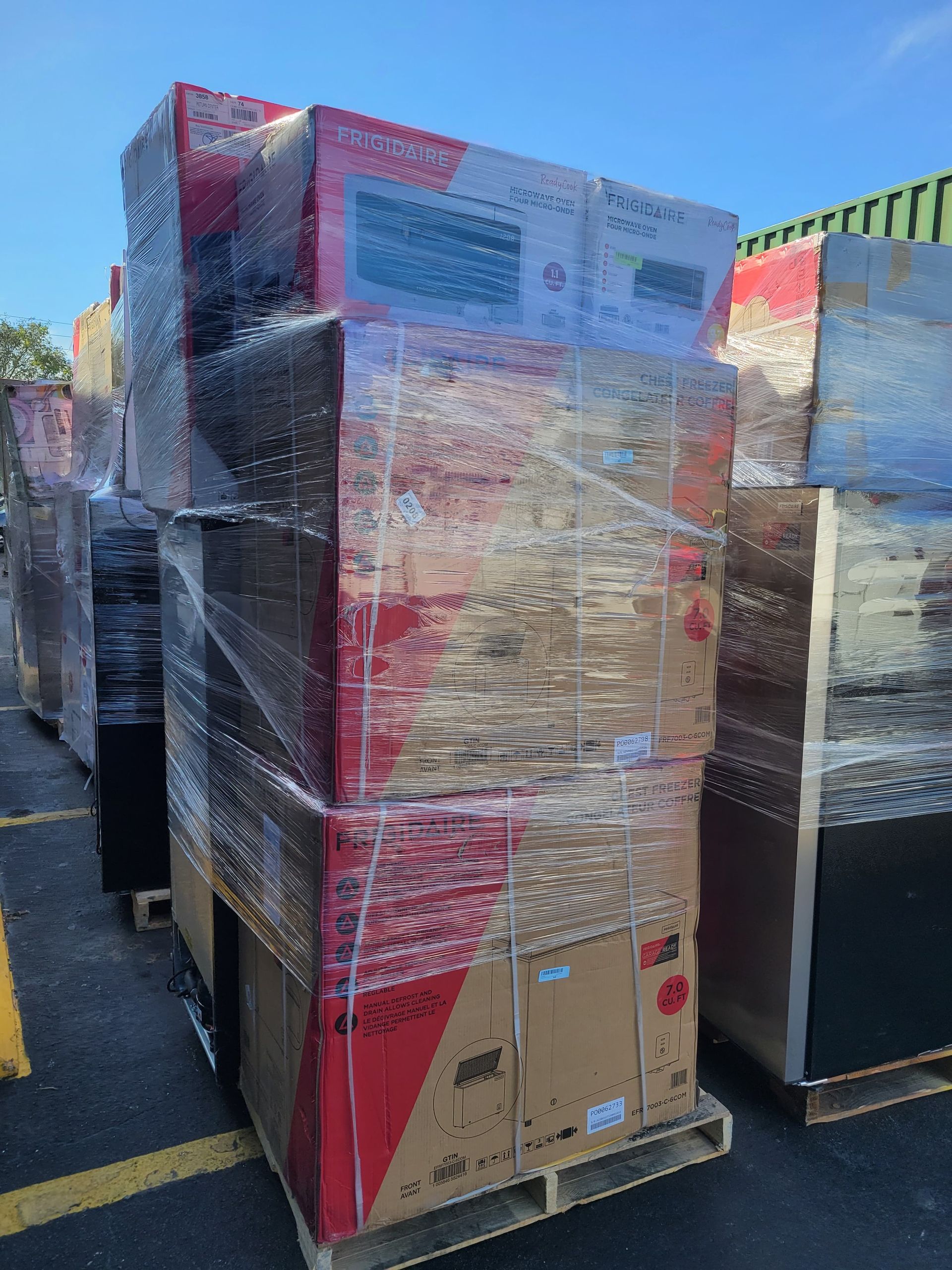 Pallets stacked with large boxes, wrapped in plastic, outdoors. Boxes have red and black designs.