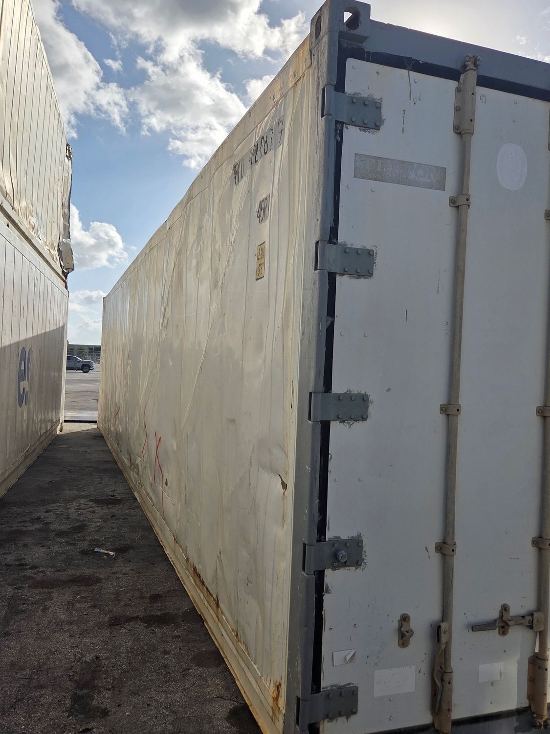 White shipping container, likely refrigerated, outdoors under a cloudy sky.