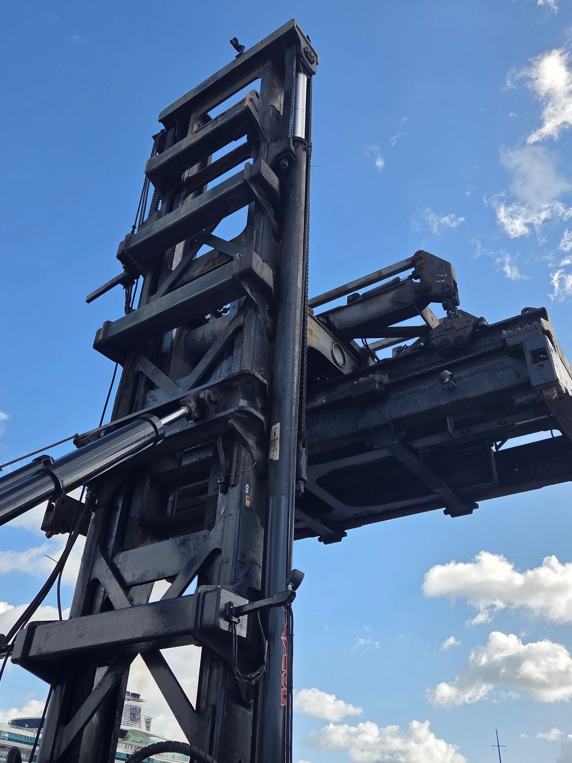 Black forklift, raised high, against a blue sky with some clouds.