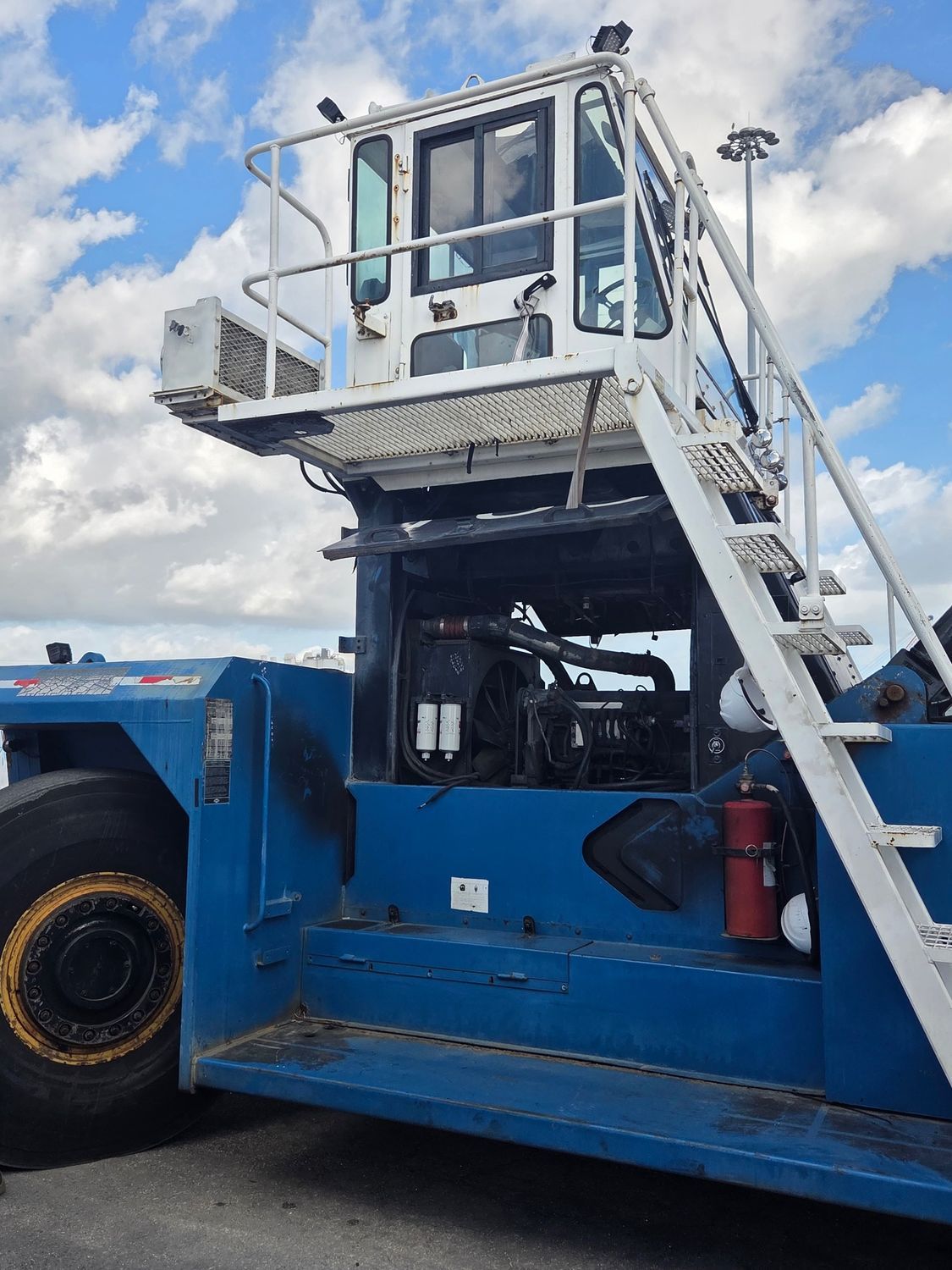Blue and white airport tow tractor with a high driver's cab and steps.