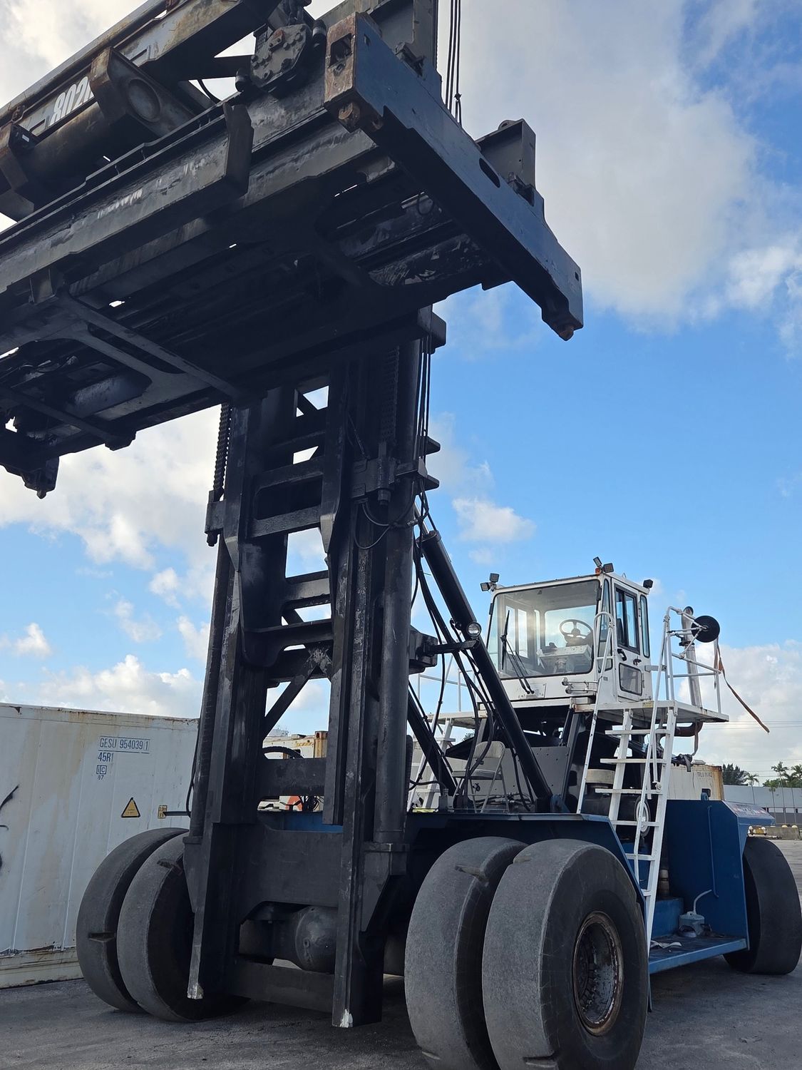 A large, dark-colored container handler against a partly cloudy sky.