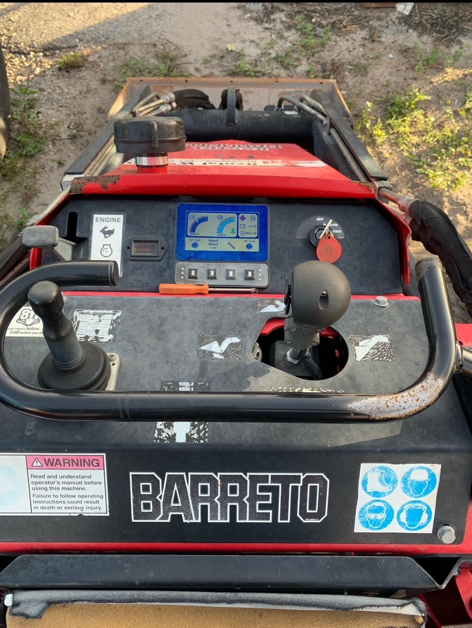 A close-up of a red Barreto trencher control panel with a joystick and display.