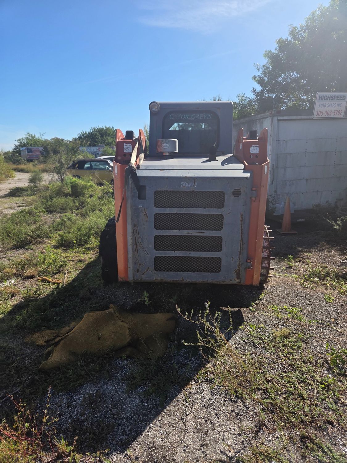 Orange and gray skid steer loader on gravel, sunny day.