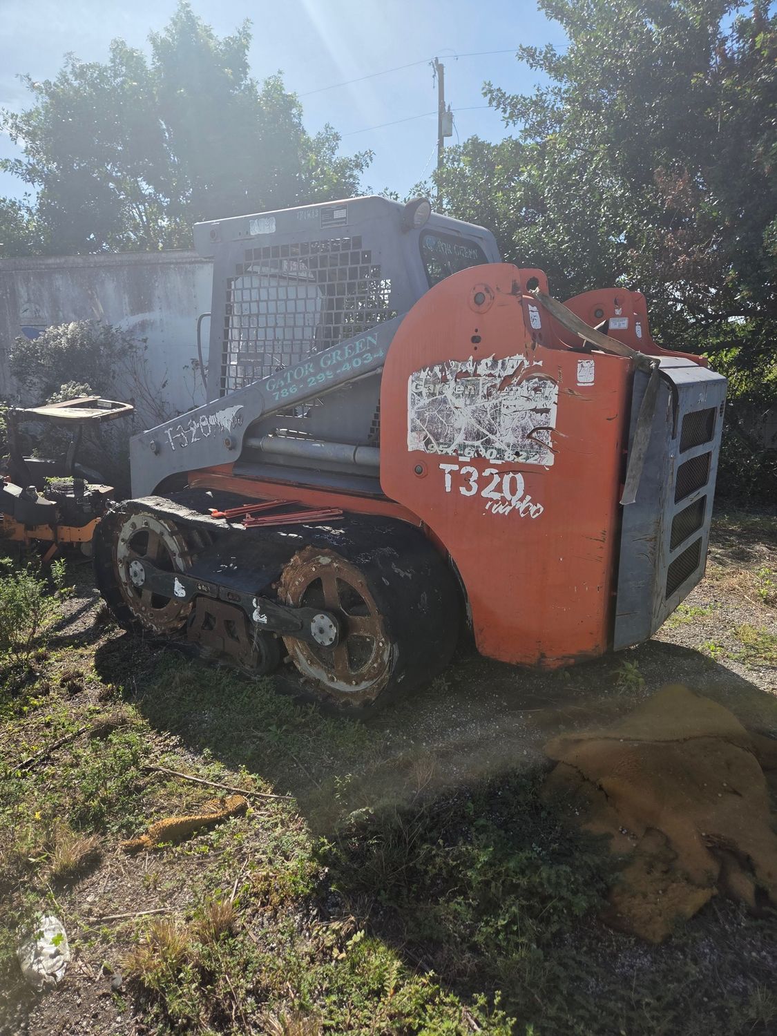 Orange and gray track skid steer loader, T320 model, on grass near a fence.