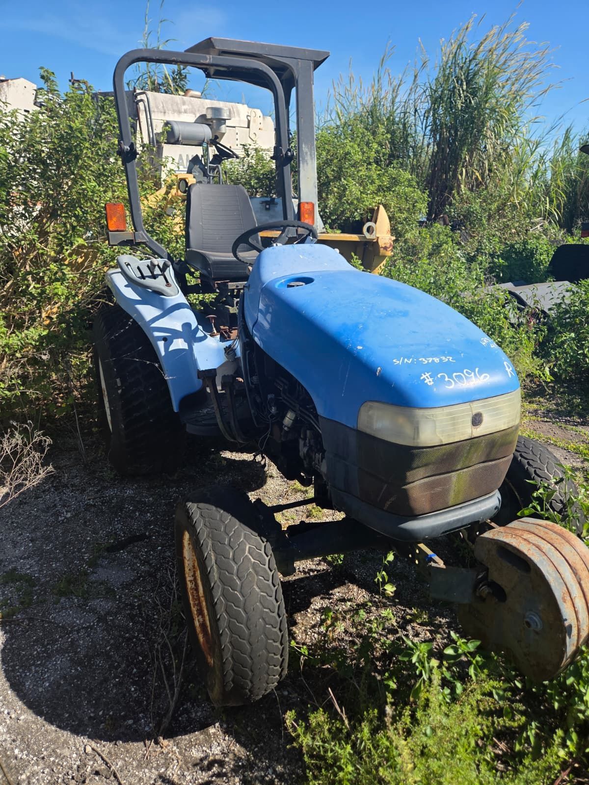Blue tractor with roll bar, parked outdoors in tall grass.