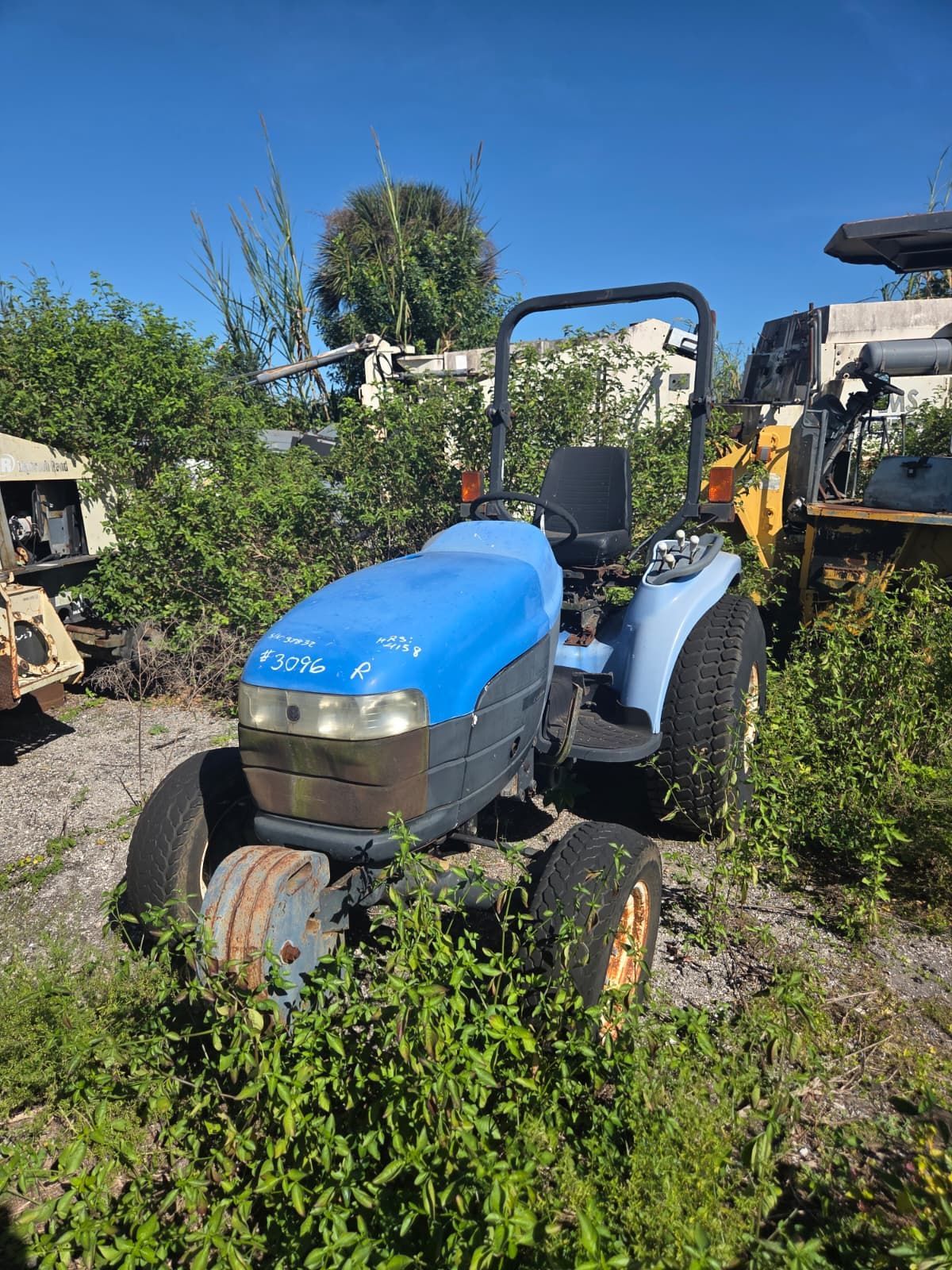 Blue and gray tractor overgrown with weeds in a junkyard.