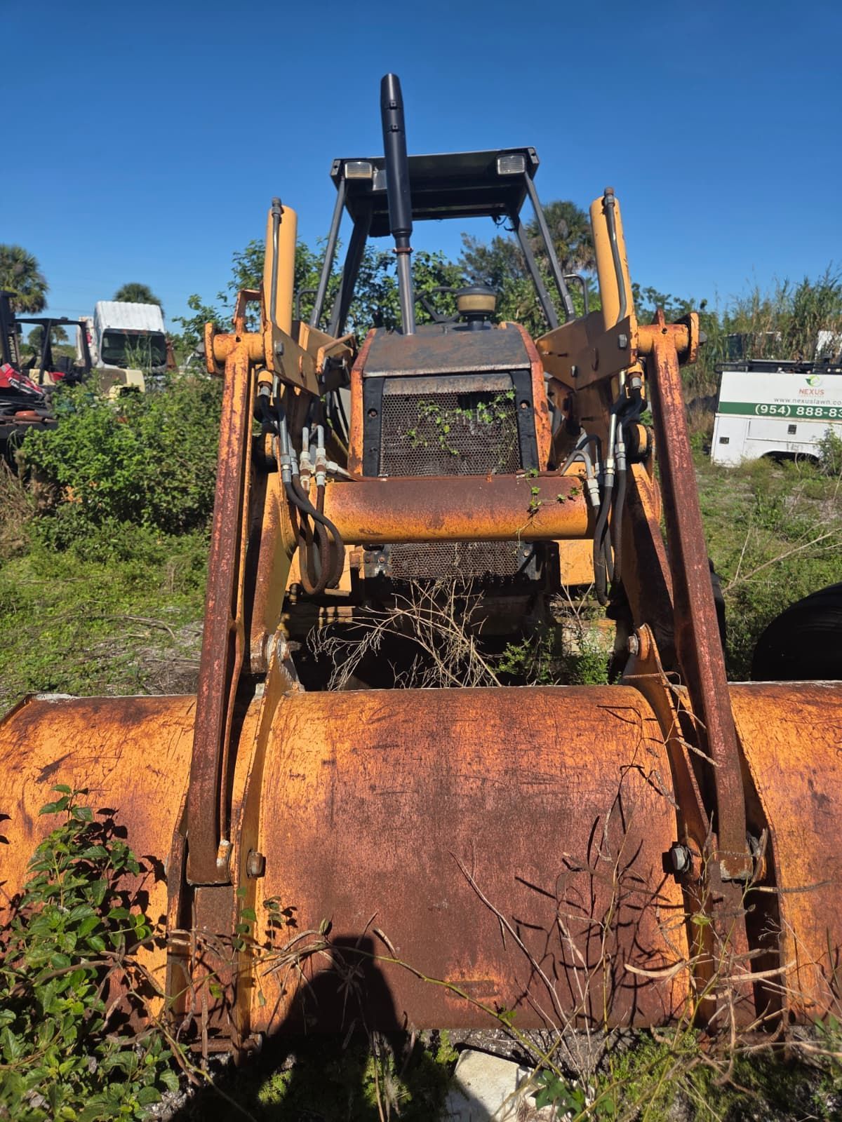 Rusty, orange tractor front end with bucket and loader arms in a field.