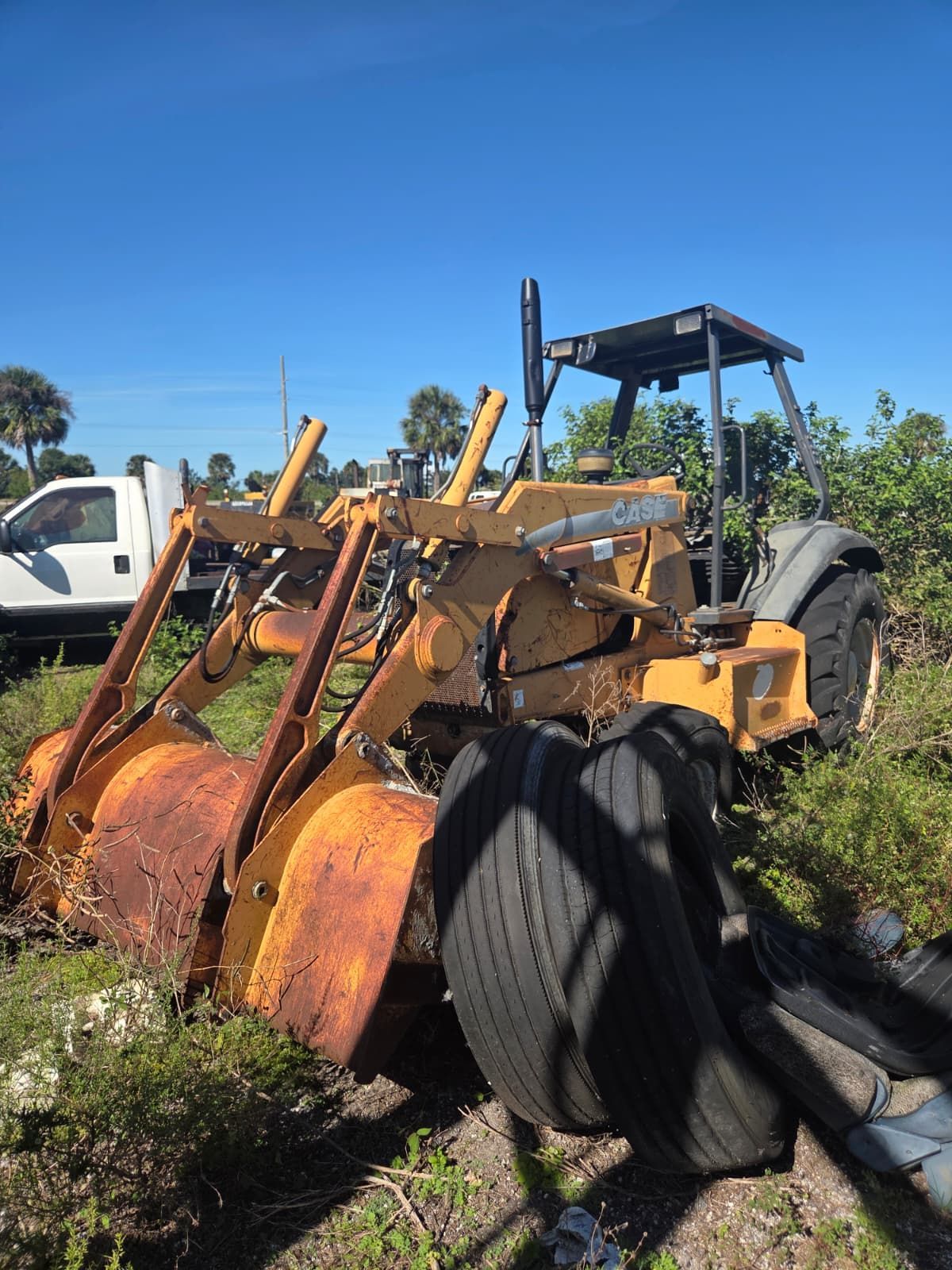 Yellow industrial tractor with a rusty bucket, tires, and a white truck in the background.