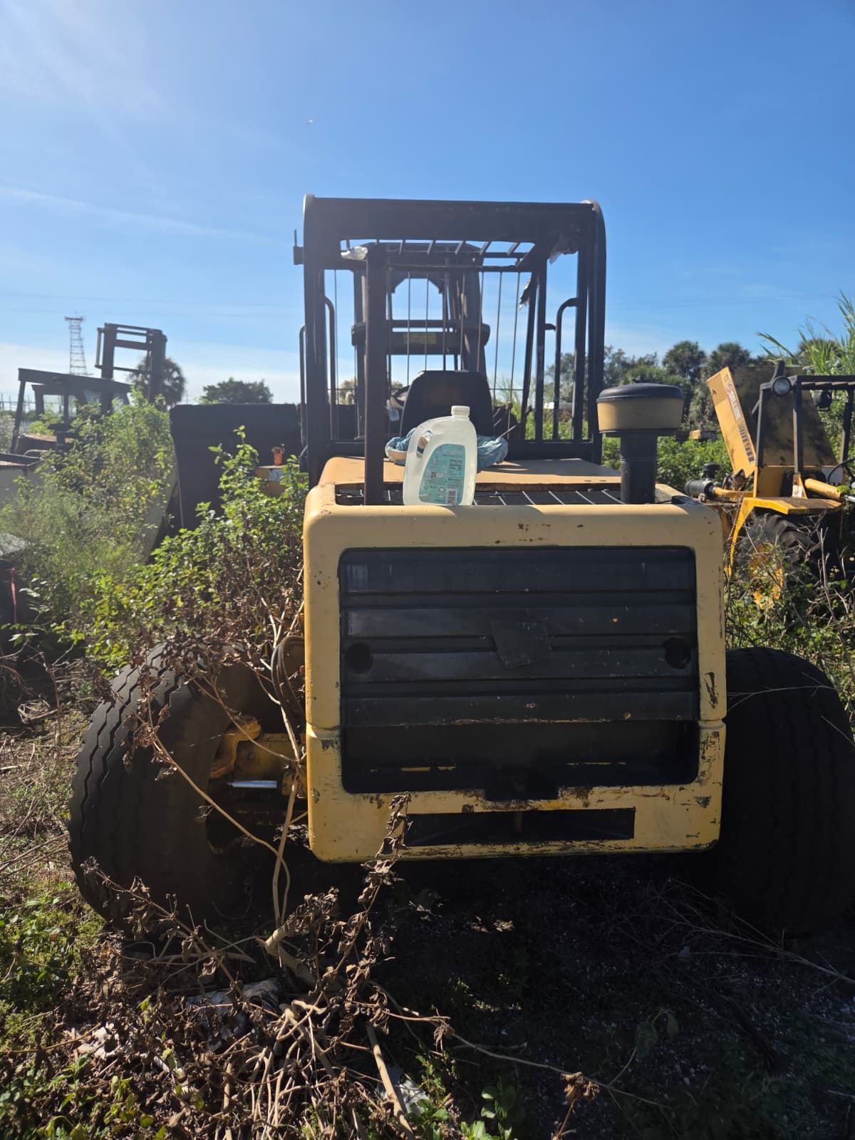 Yellow and black heavy machinery overgrown with weeds under a clear sky.