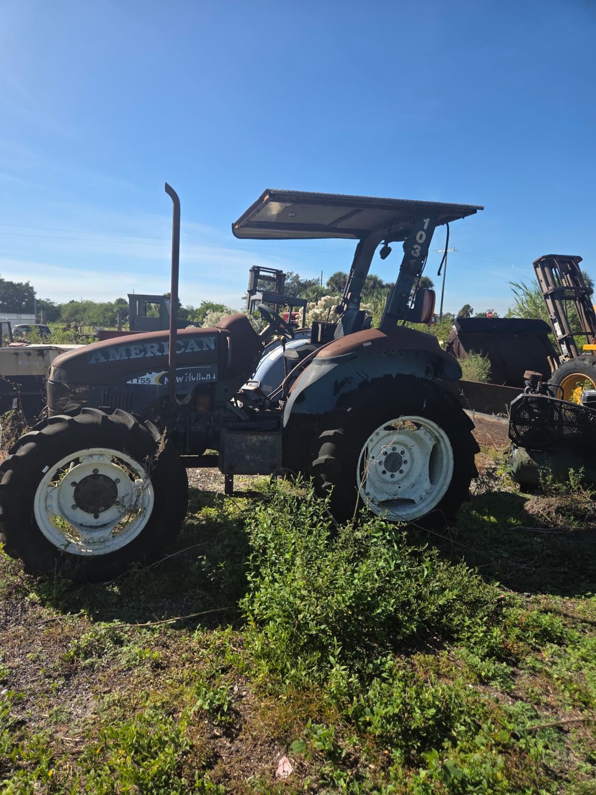 A weathered blue tractor with white wheels and a canopy, parked in a grassy field on a sunny day.