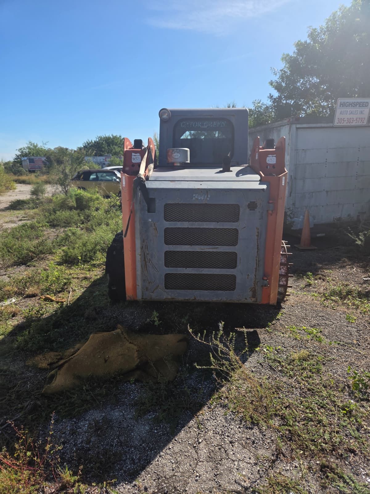 Orange and gray skid steer loader parked on gravel.
