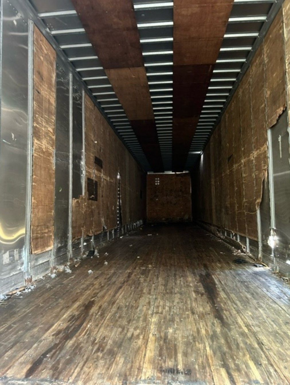 Interior of a semi-trailer. Worn wooden floor and walls, metal beams overhead.