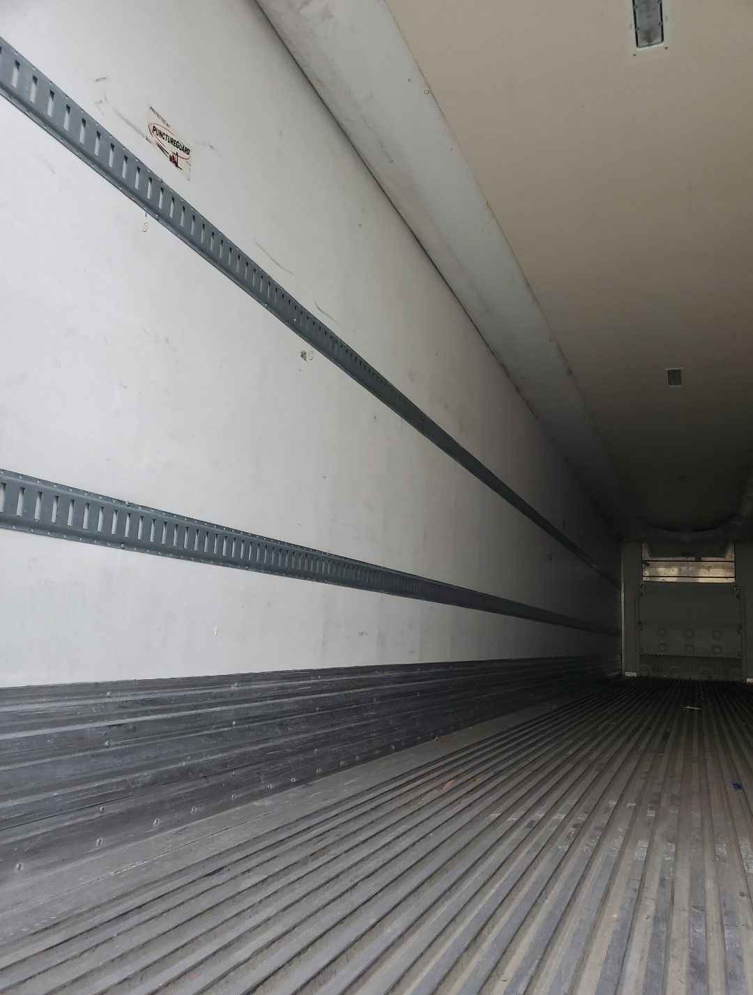 Interior of a semi-trailer with gray and white walls and ribbed floor.