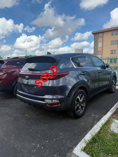 Dark gray Kia Sportage SUV parked in a lot, with a building and sky visible in the background.