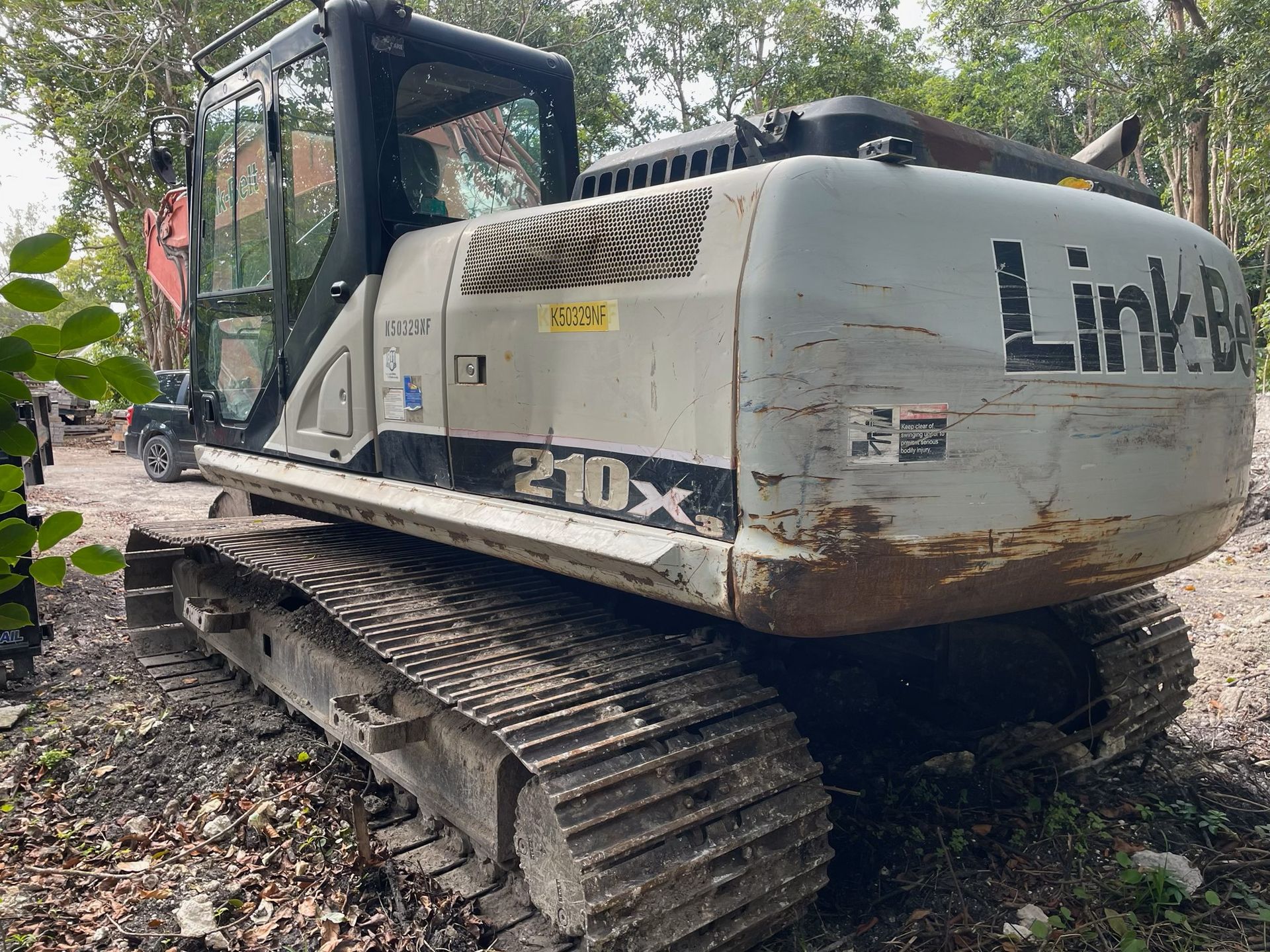 Gray Link-Belt 210X excavator parked outdoors in a wooded area.
