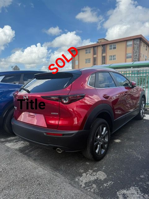 Red Mazda CX-30 SUV parked outdoors with a blue sky background and a building.