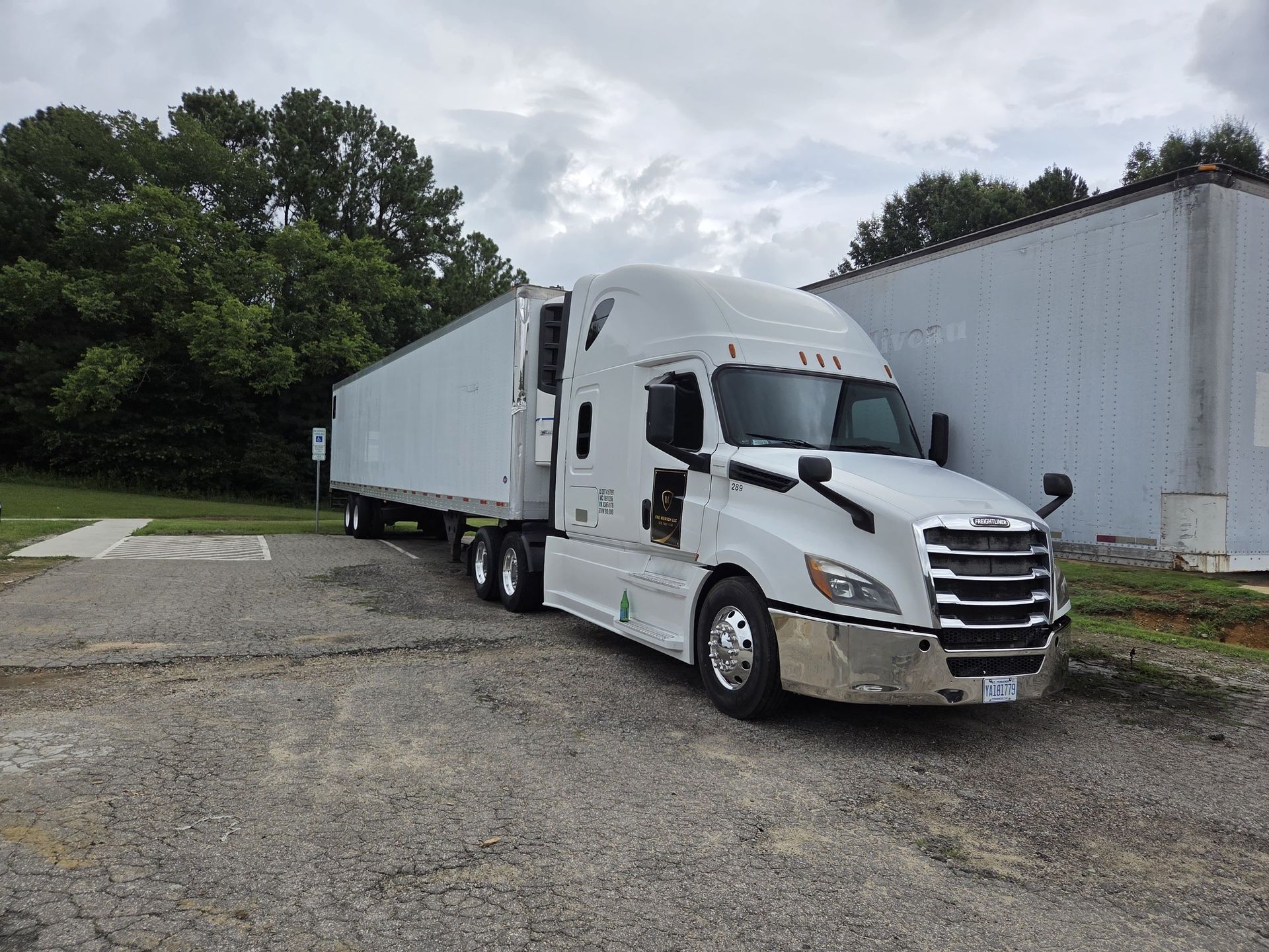 White semi-truck parked on gravel near a building and trees on a cloudy day.