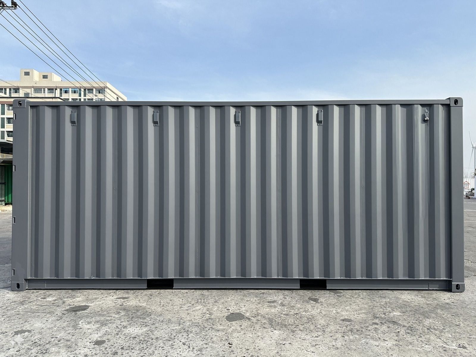 Gray shipping container on a concrete surface against a light blue sky.
