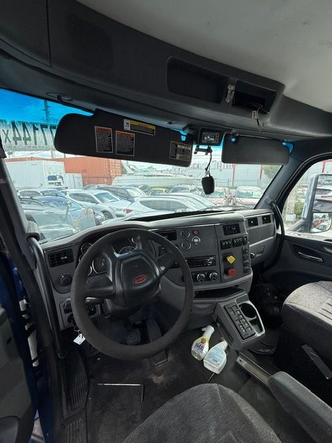 Interior of a truck cab, including steering wheel, dashboard, sun visors, and a view of parked cars through the windshield.