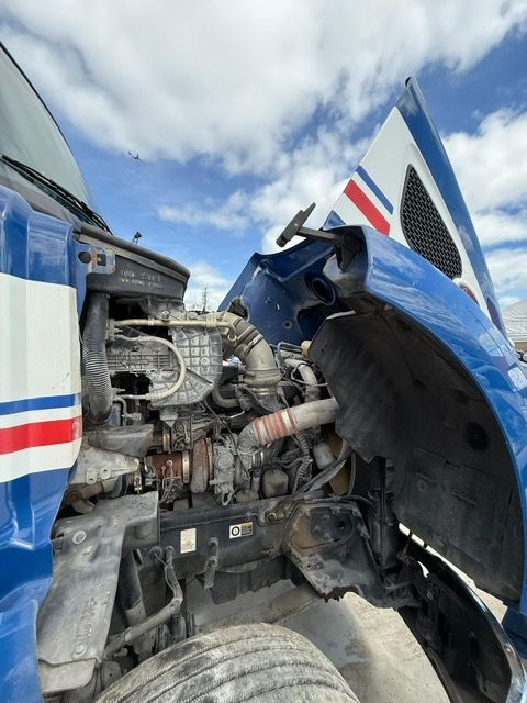 Semi-truck engine compartment with the hood open, against a cloudy sky.