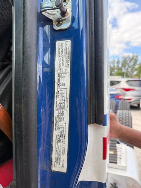 Blue car door frame with white sticker containing vehicle information. A hand touches the frame.
