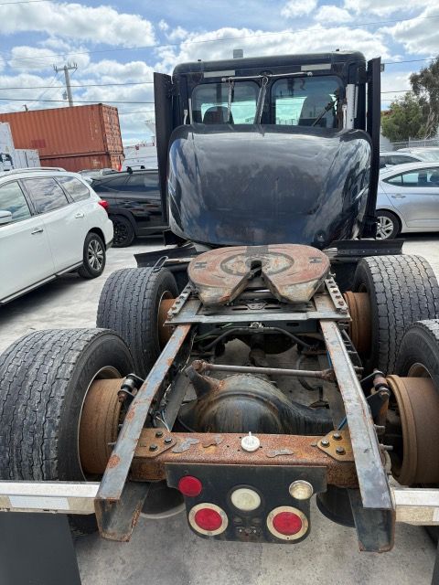 Rear view of a black semi-truck cab and chassis with a fifth wheel hitch.