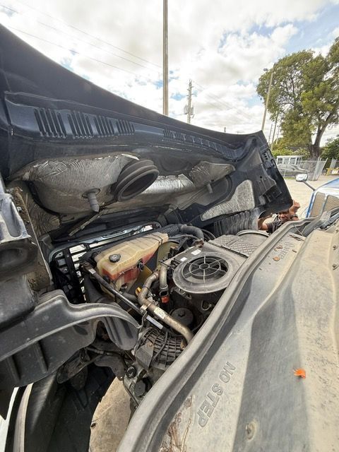 Open truck hood, revealing engine. Grey, black, and red components. Outdoors, sunny day.
