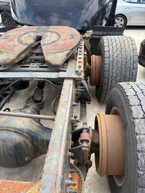 Undercarriage of a rusty semi-truck. The fifth wheel hitch, tires, axles, and frame are visible.