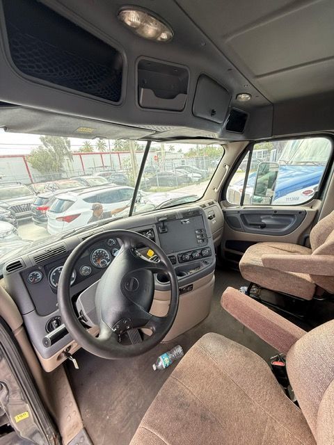 Interior of a truck cab, including the steering wheel, dashboard, seats, and windshield.