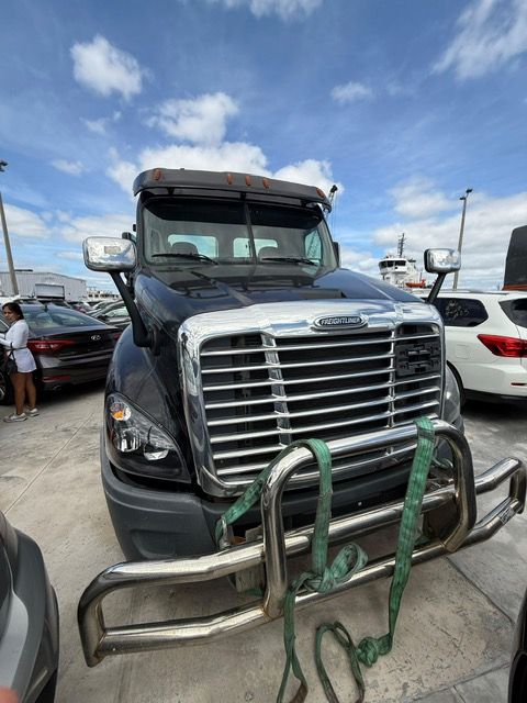 Black Freightliner truck with chrome grill and bumper, secured with green straps, outdoors under a cloudy sky.