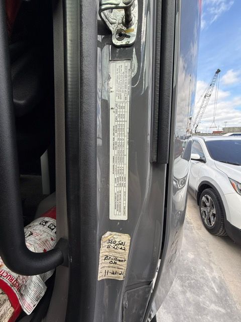 Door jamb with a vehicle information sticker and a smaller sticker below. Gray car exterior in background.