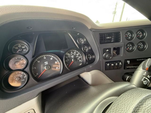 Dashboard of a semi-truck with multiple gauges, a speedometer, and various controls, in a gray interior.