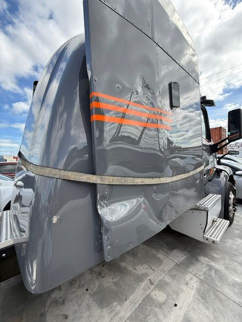 Damaged gray semi-truck cab with orange stripes and dented side panels parked outside.