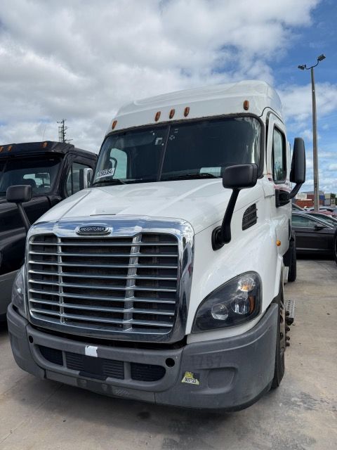 White Freightliner semi-truck parked outdoors, front view. Gray bumper, chrome grille, black side mirrors, cloudy sky.