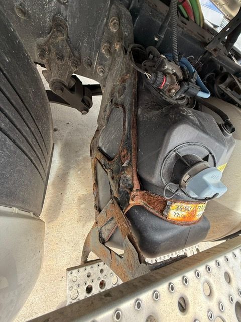 Close-up view of a truck's DEF fluid tank secured with rusty metal straps.