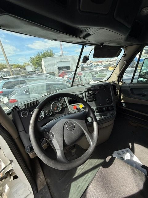 Interior of a truck cab, including steering wheel, dashboard, and windshield; outdoors, with other vehicles visible.