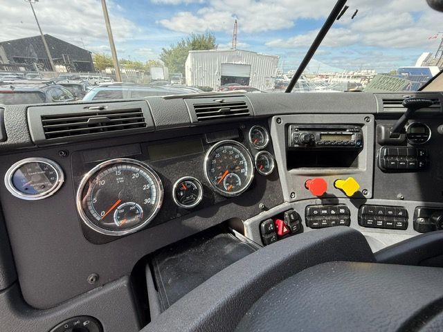 Dashboard of a semi-truck with gauges, radio, and control buttons; overcast sky visible through windshield.