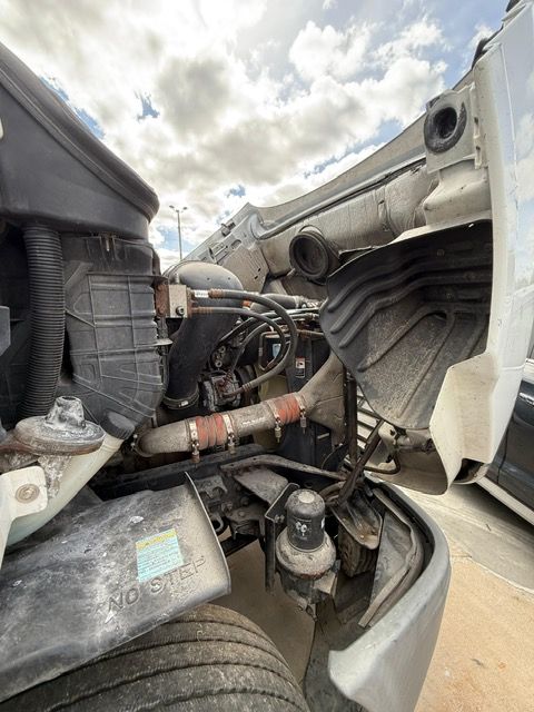 Open hood of a semi-truck showing engine components under a cloudy sky.