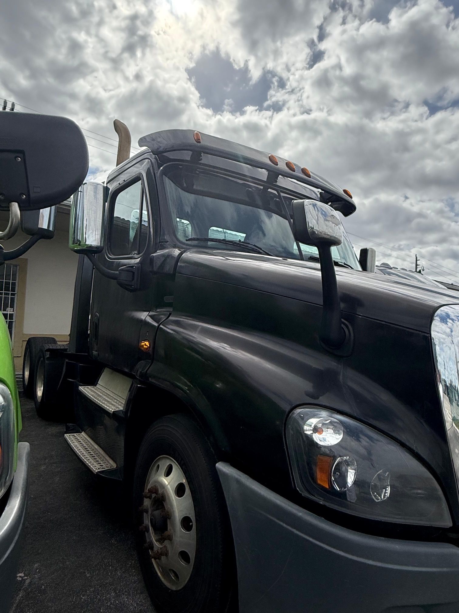 Black semi-truck parked outside on a cloudy day.