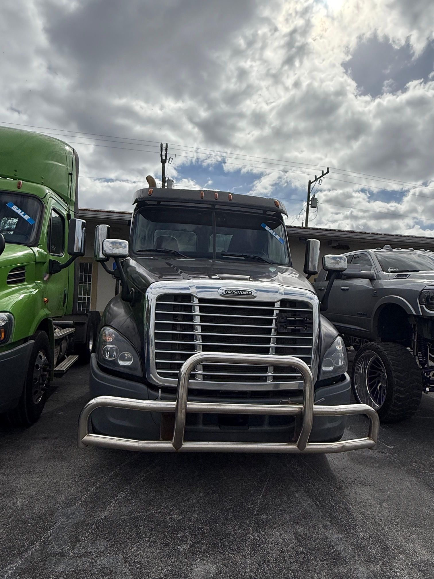 Dark gray semi-truck with a chrome grill guard, parked outdoors on a cloudy day.