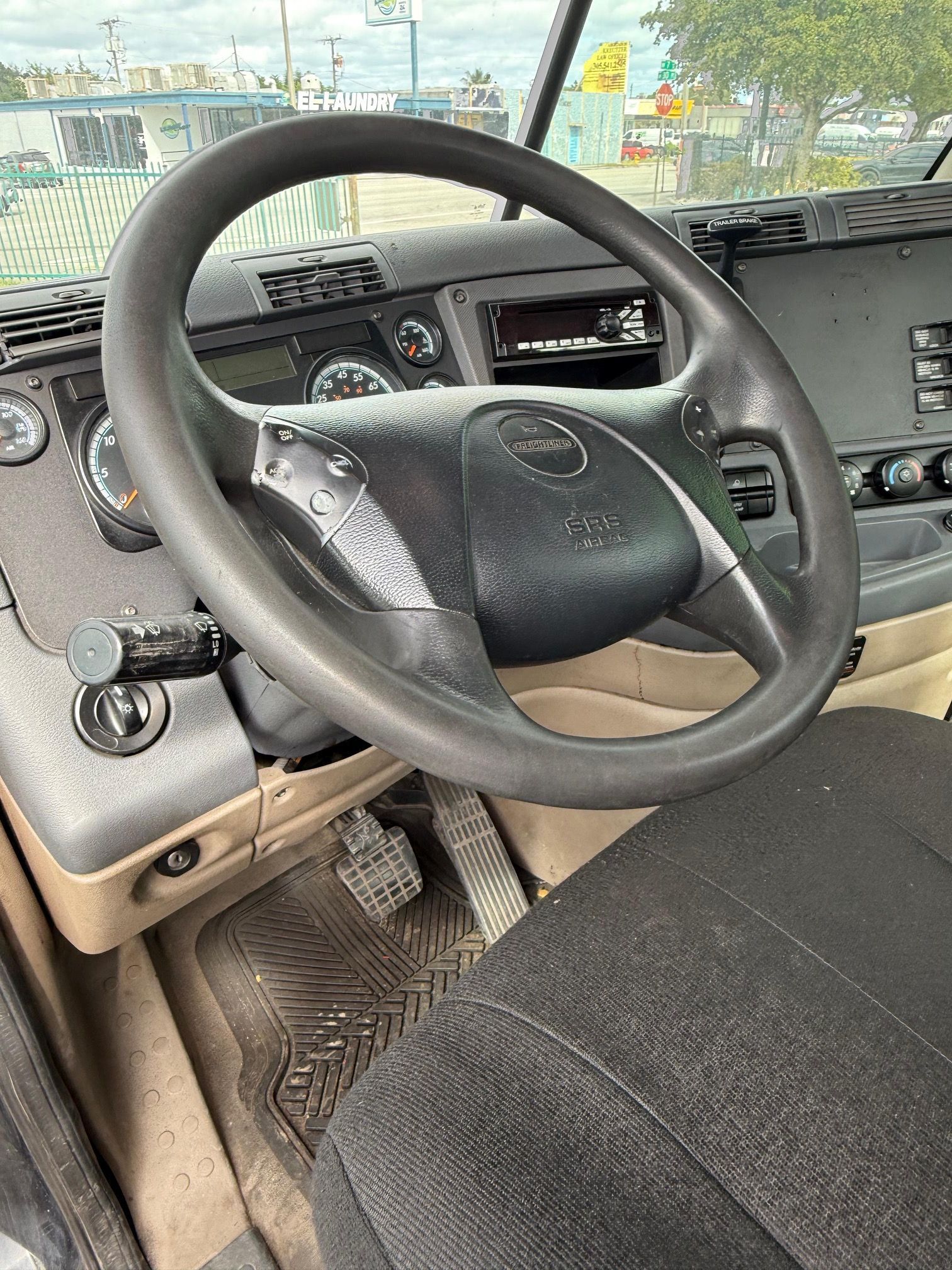 Interior view of a truck cab, showing a black steering wheel, dashboard, seat, and pedals.