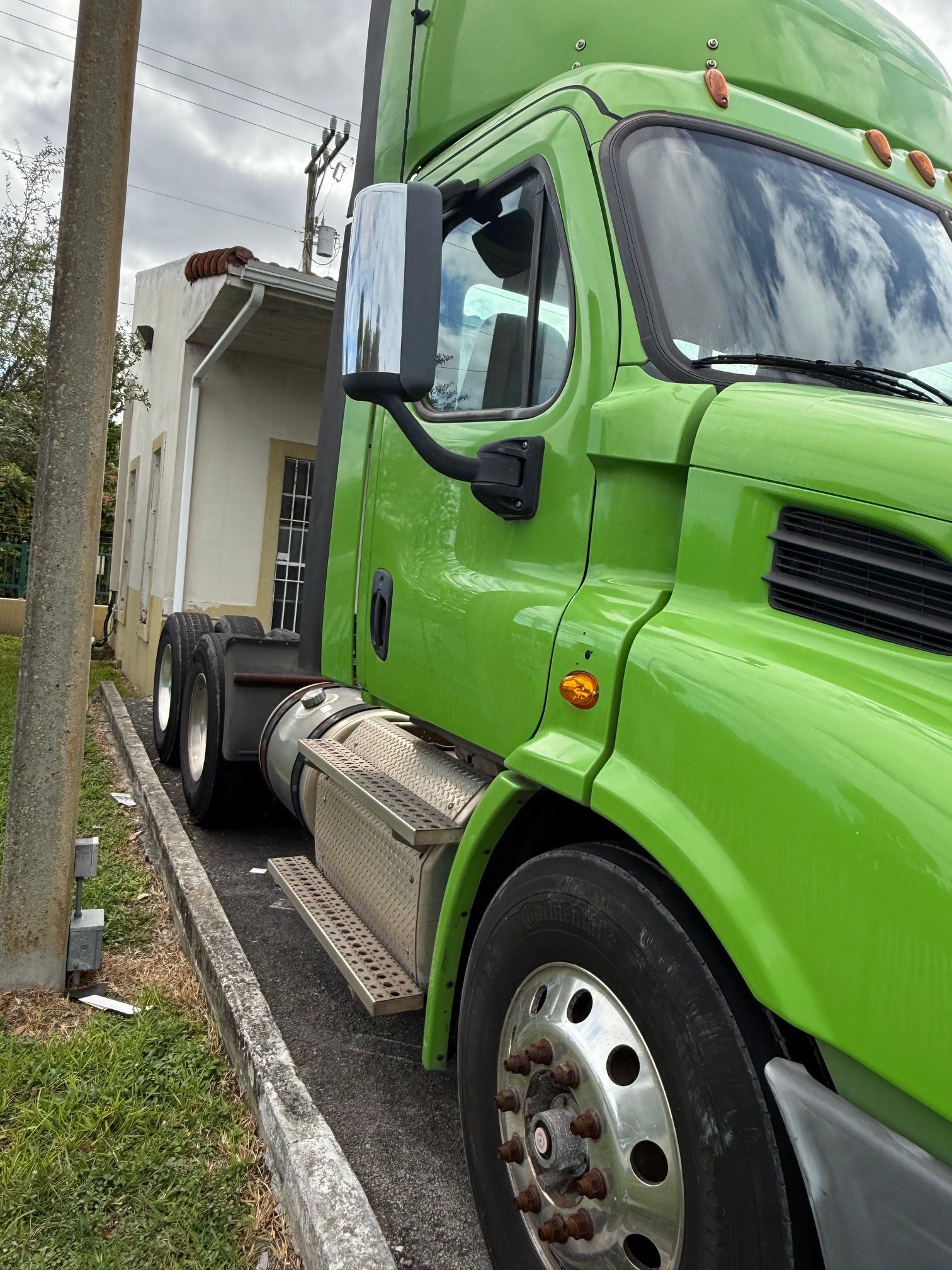 Green semi-truck parked next to a building on a curb. Cloudy sky.