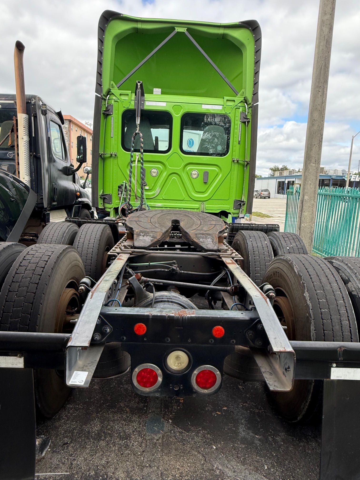 Back view of a green semi-truck cab with its hitch exposed. Gray metal frame and black tires.