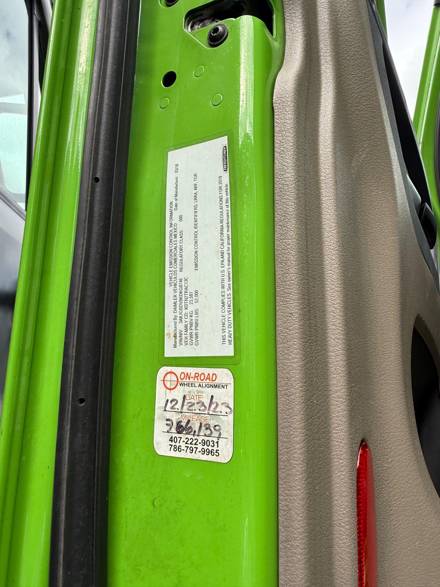 Green car door frame with a sticker detailing vehicle information.  An inspection sticker is also present.