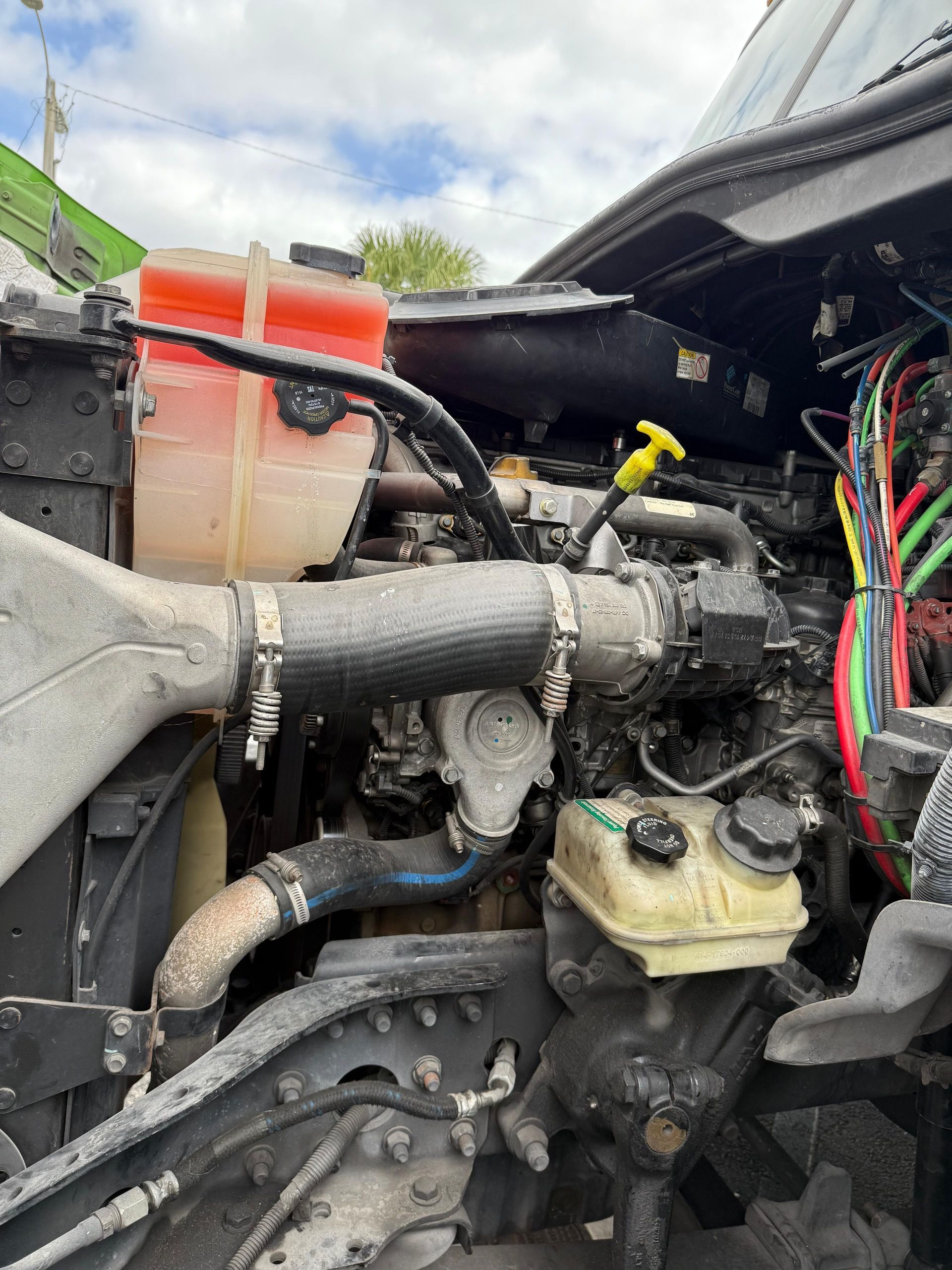 Engine compartment of a semi-truck with coolant reservoir, hoses, and various components.