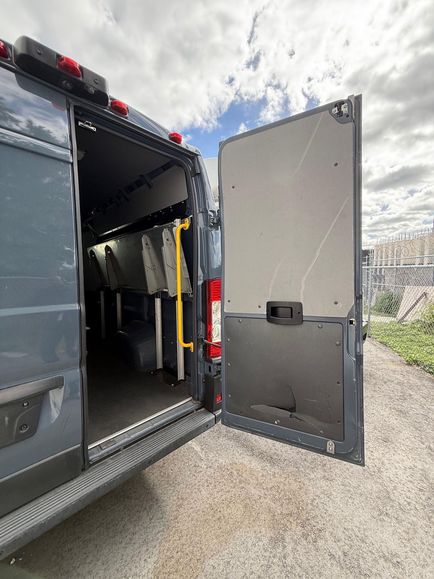 Dark gray van with open back doors, revealing interior seating and a yellow handrail.